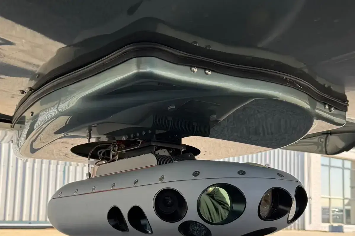 Close view of a streamlined camera housing with several lens openings, mounted under an aircraft