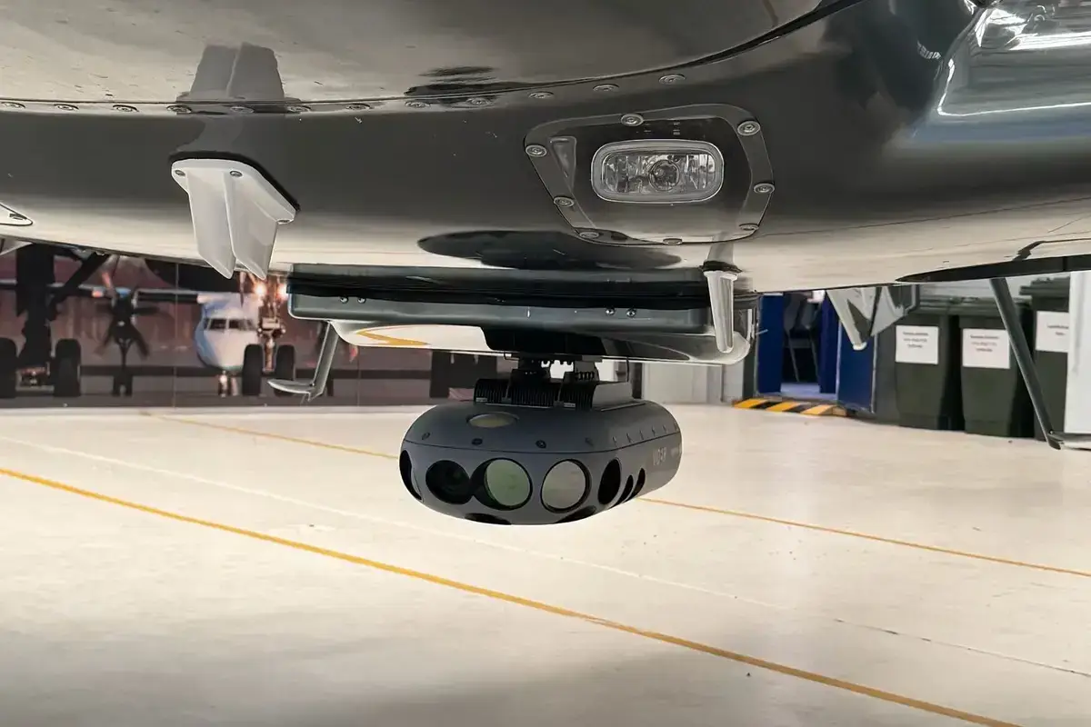 The underside of an aerial survey aircraft in a hangar, with the camera housing mounted beneath it
