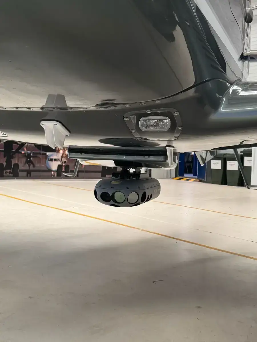The camera housing mounted under the fuselage of an aerial survey aircraft, seen from the hangar floor