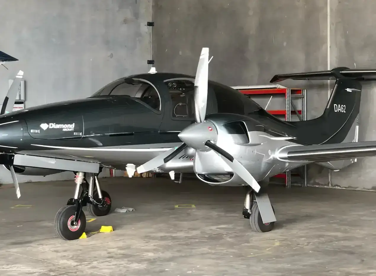 A charcoal and silver Diamond DA62 twin-engine aircraft parked in a concrete hangar
