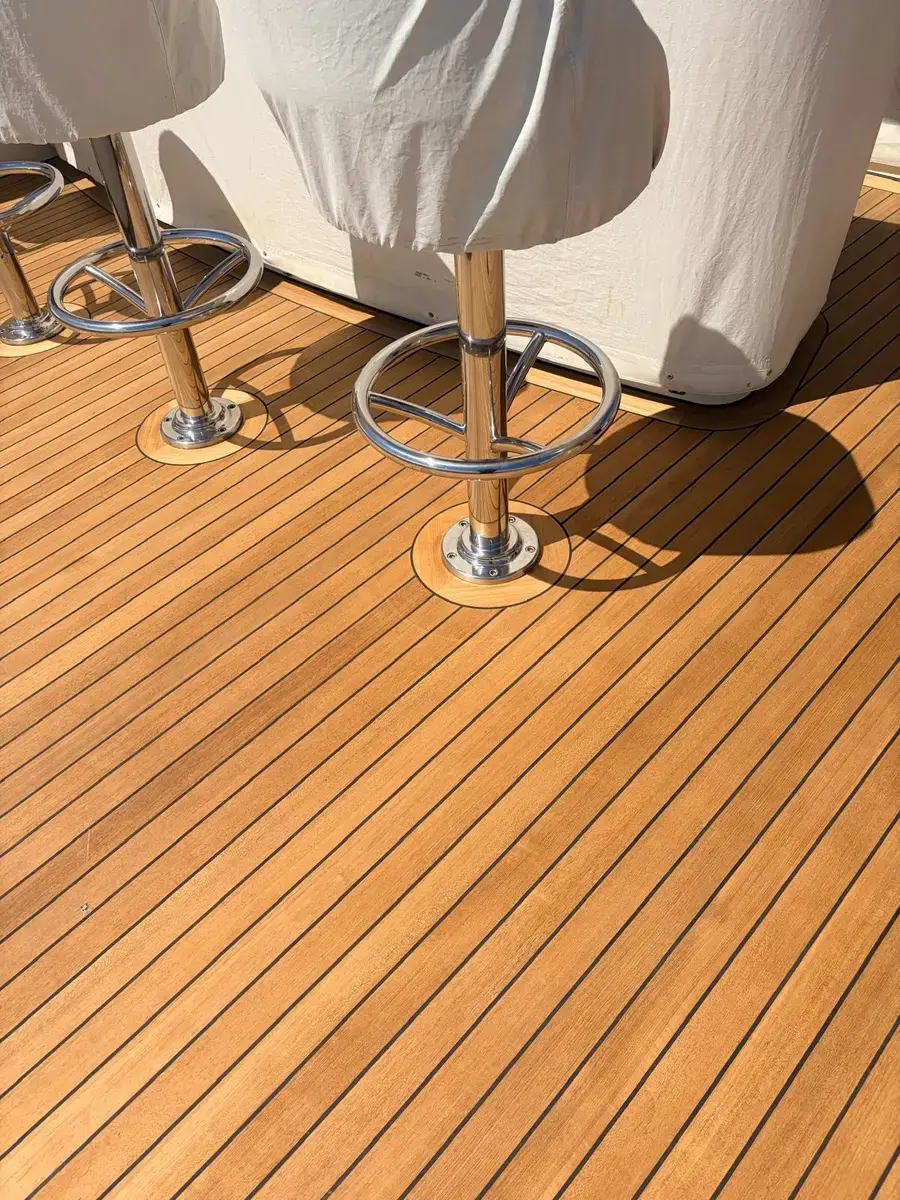 A newly finished teak deck with dark seams and inset margins around stainless pedestal fittings