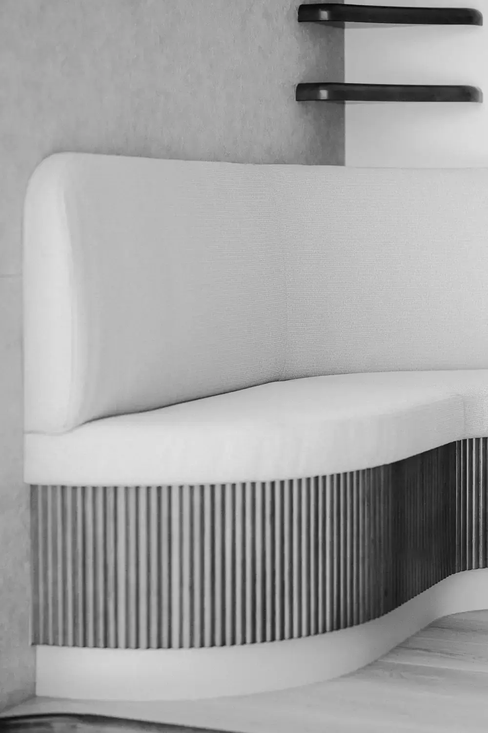 Black and white detail of the curved banquette, its upholstered seat and back running over a fluted timber base