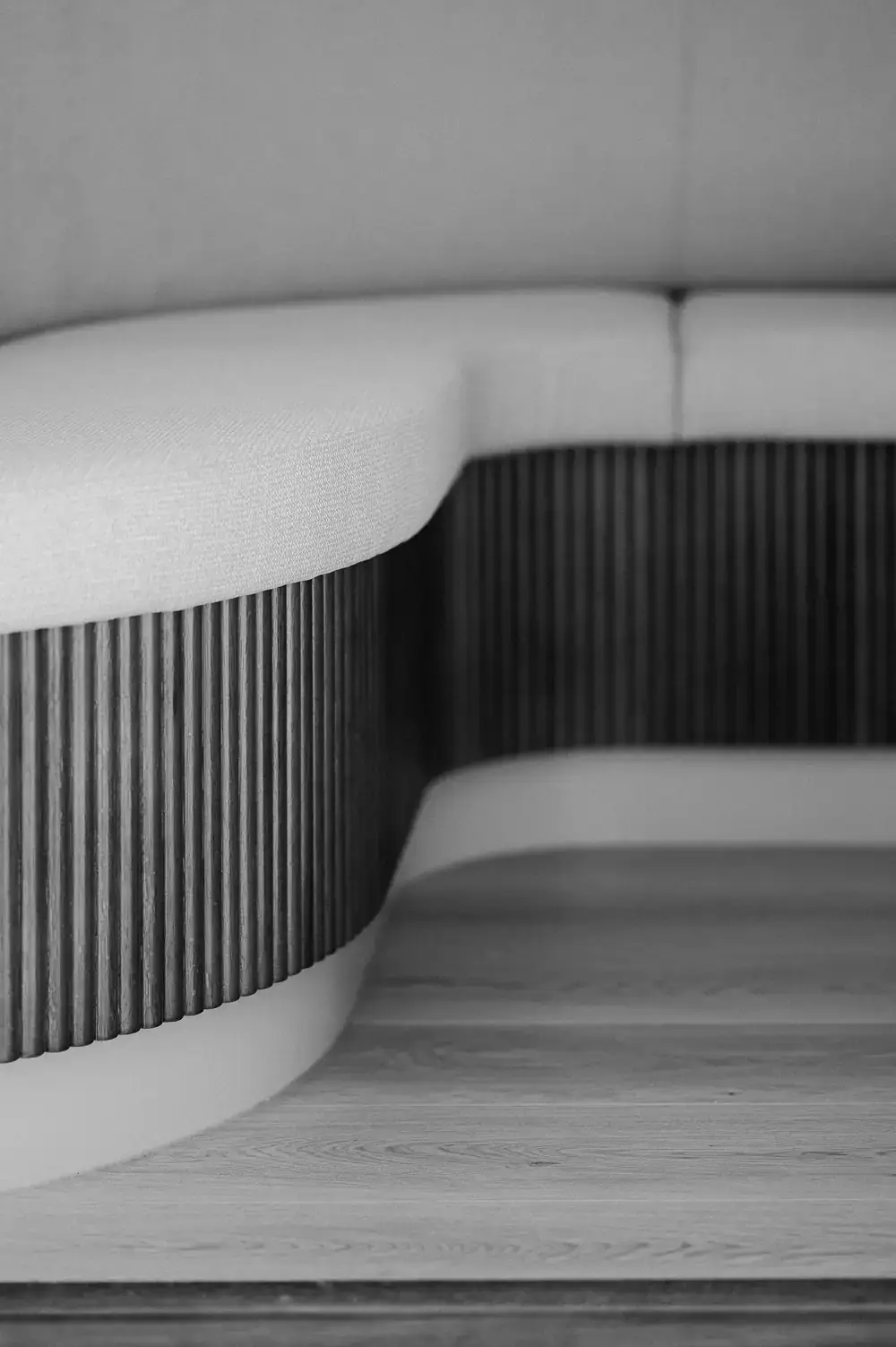 Black and white close view of the banquette's fluted timber base turning a curve beneath the upholstered seat