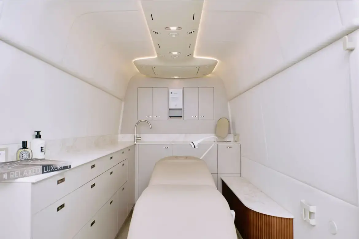 The white treatment area inside the Sprinter, with a treatment bed, stone-look work surfaces, fitted cabinetry and a lit ceiling