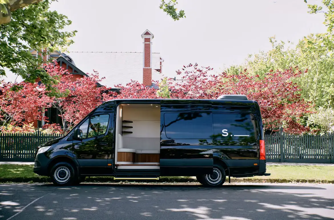 The black SKN.JECT Sprinter parked on a tree-lined street, side door open to its light interior